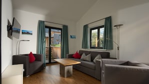 Un salon moderne avec deux canapés, une table basse, un téléviseur fixé au mur et une vue sur l’extérieur.