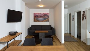 A modern living room with a sofa, a coffee table, a TV mounted on the wall, and a painting above the sofa. - 4802 Cirrus 2 (St. Gallenkirch)