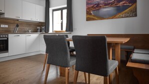 Une cuisine moderne avec des meubles blancs, un plan de travail en bois et un coin repas comprenant une table en bois et des chaises à revêtement gris.