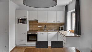 Une cuisine moderne avec des meubles blancs, un plan de travail en bois, un four encastré et un coin repas avec deux chaises.