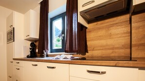 A kitchen with white cabinets, a wooden countertop, and a window with brown curtains. - 47021 Kollin 2 EG (St. Gallenkirch)