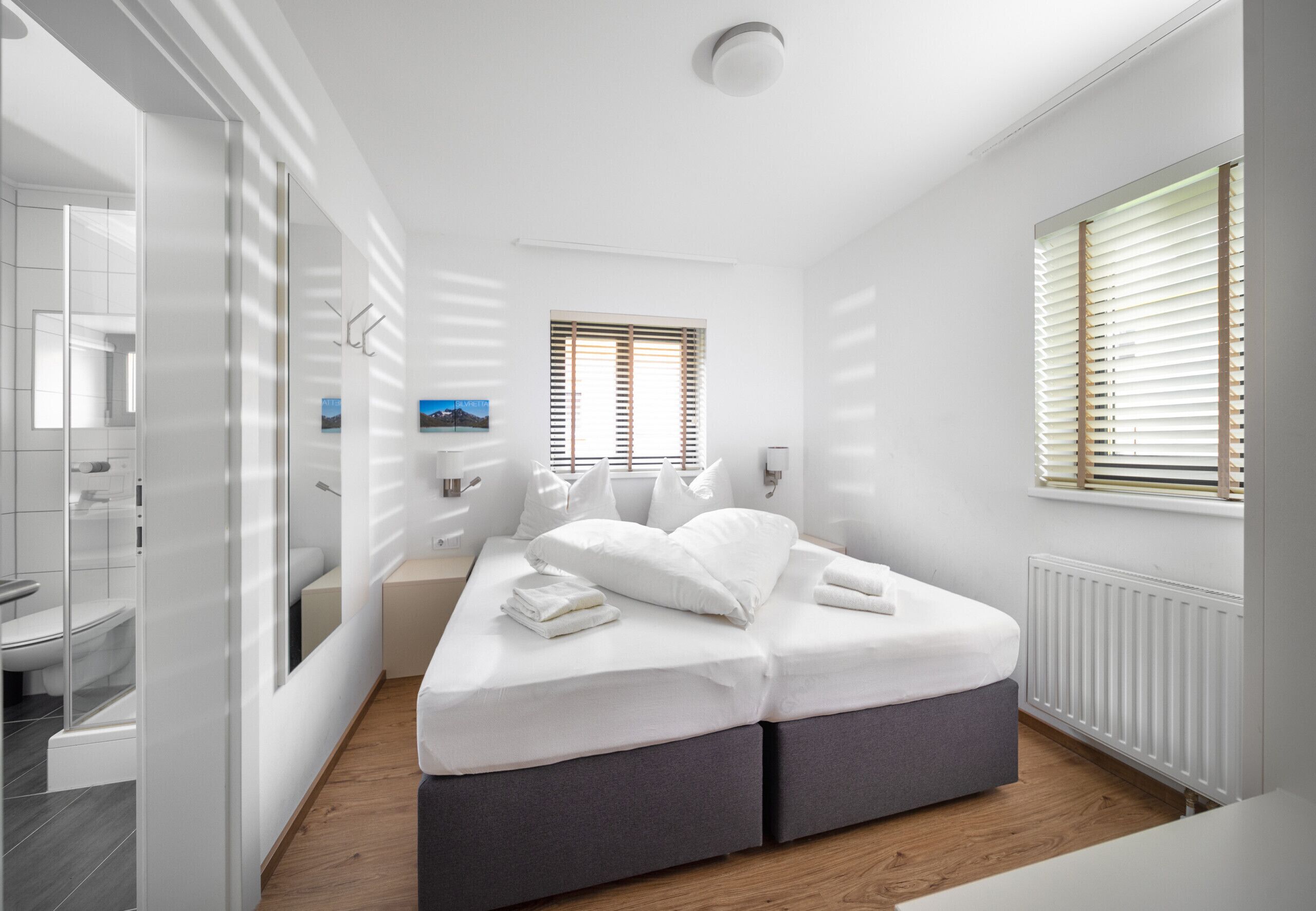 A modern bedroom with a bed, bedside tables, and a view of the outside through a window.