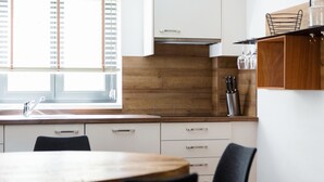 Eine moderne Küche mit Holzauszug, weißen Schränken und einem Fenster mit Jalousien.
