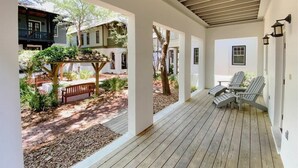 A covered porch with wooden flooring, white walls, and a view of a garden with a bench and Adirondack chairs. - Sky Pool/Heated, Fitness & Tennis Center-4 Bikes (Panama City Beach)