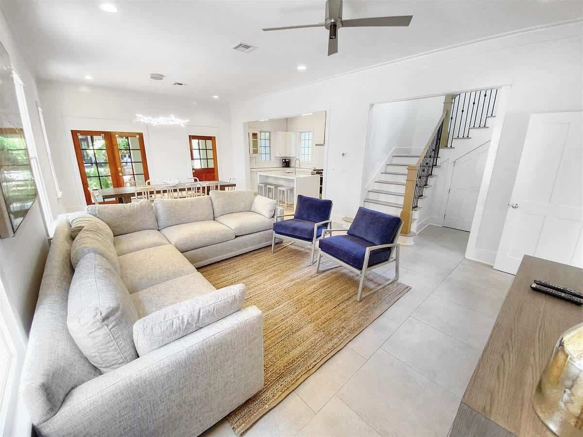 Ein modernes Wohnzimmer mit einer Couch, Sesseln, einem Teppich und einer Treppe.