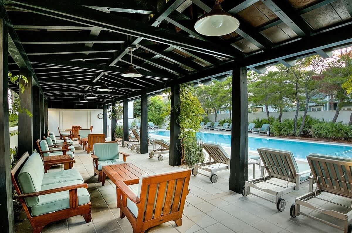 A covered outdoor seating area with wooden furniture and a view of a swimming pool.