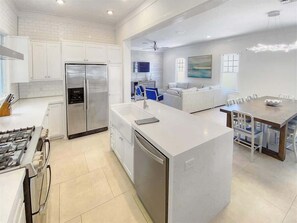 Cozinha moderna com ilha central, eletrodomésticos de aço inoxidável e área de jantar com mesa e cadeiras.