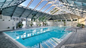 An indoor swimming pool with a glass ceiling, surrounded by lounge chairs and potted plants. - Sky Pool/Heated, Fitness & Tennis Center-4 Bikes (Panama City Beach)