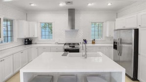 A modern kitchen with white cabinetry, a large island with bar stools, a stainless steel refrigerator, and a built-in oven. - Sky Pool/Heated, Fitness & Tennis Center-4 Bikes (Panama City Beach)