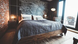 Une chambre moderne avec un grand lit, un mur décoré d’une carte, un mur en briques et une vue sur l’extérieur.