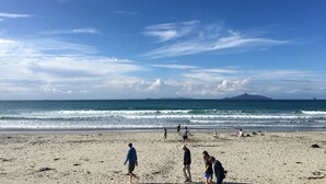 A beach with people walking and sitting, waves crashing, and mountains in the distance.