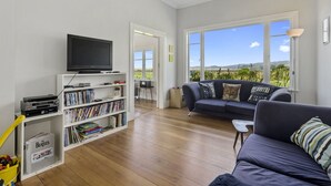 A modern living room with a flat-screen TV, bookshelves, a sofa, and a large window offering a view of the outdoors.