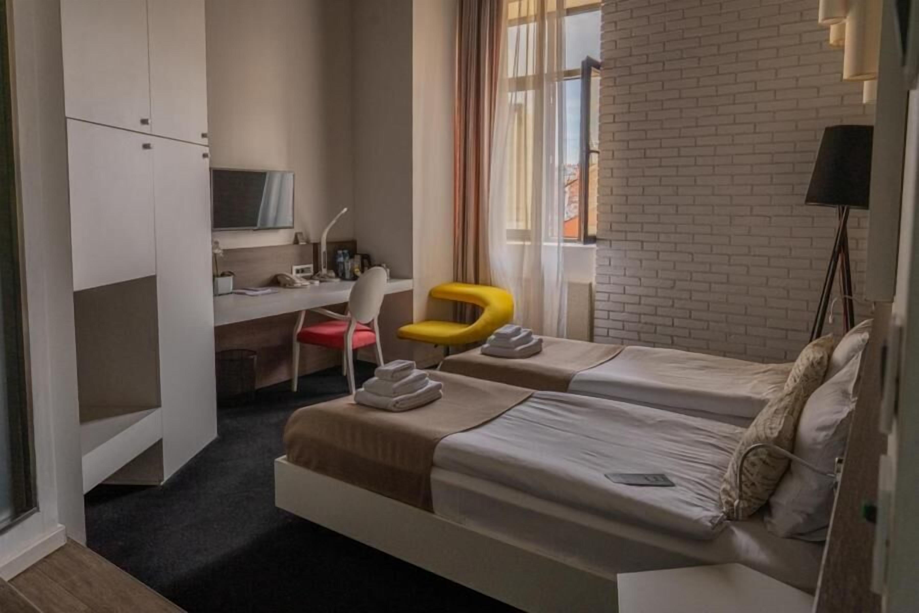 A hotel room with two beds, a desk, a chair, and a TV.