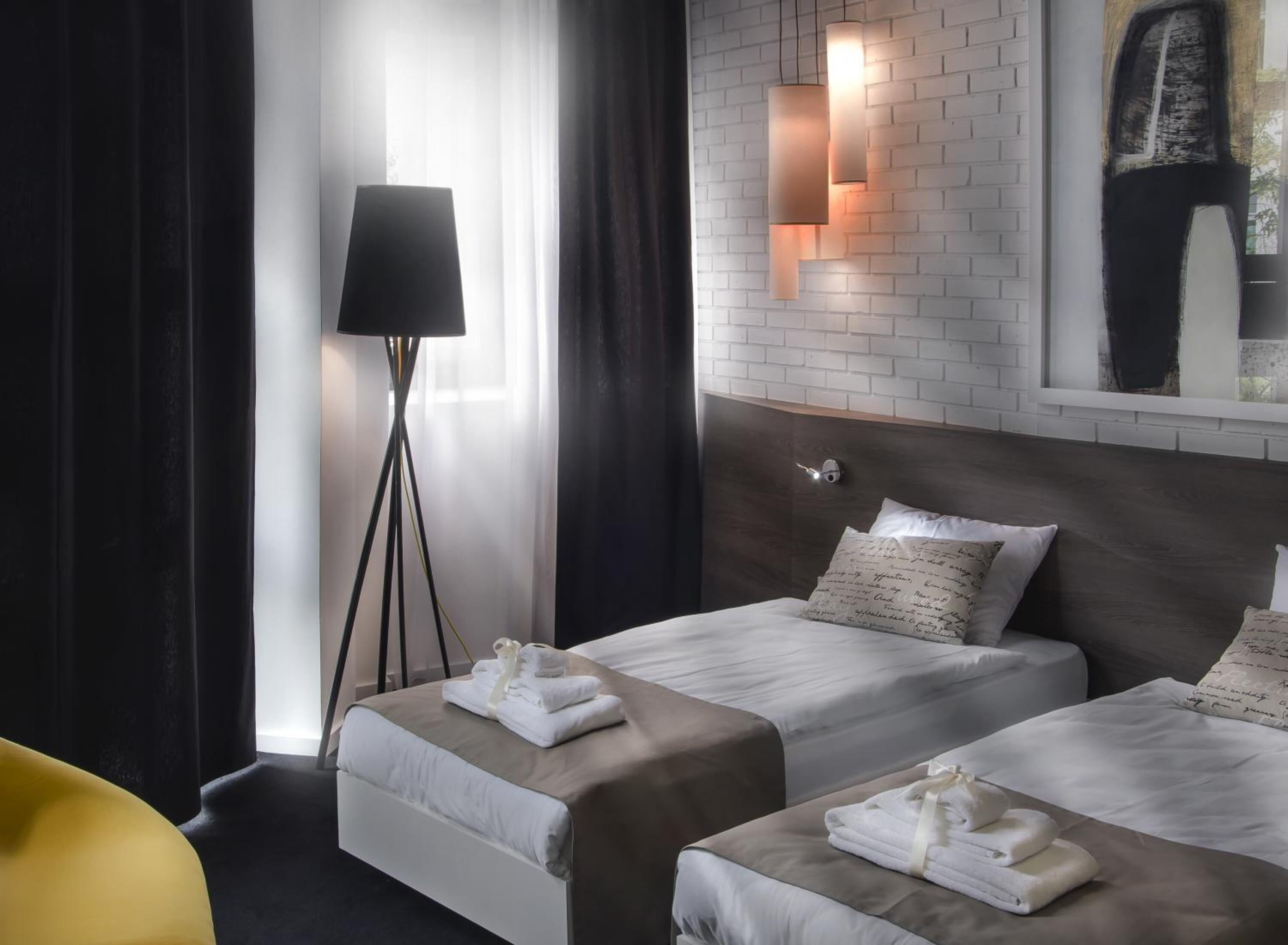 A hotel room with two beds, a floor lamp, a mirror, and a brick wall.