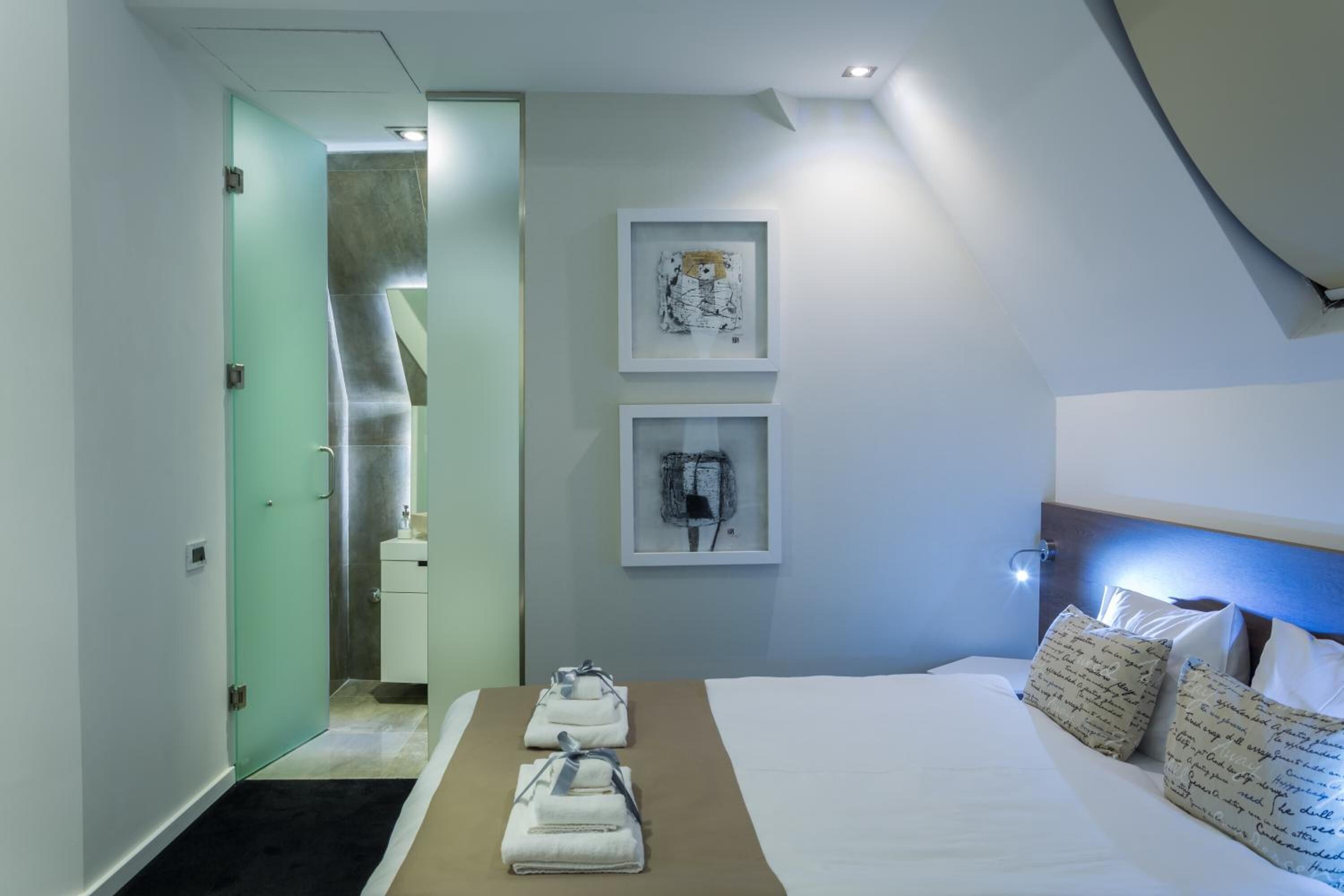 A hotel room with a bed, a nightstand, a mirror, and artwork on the wall.
