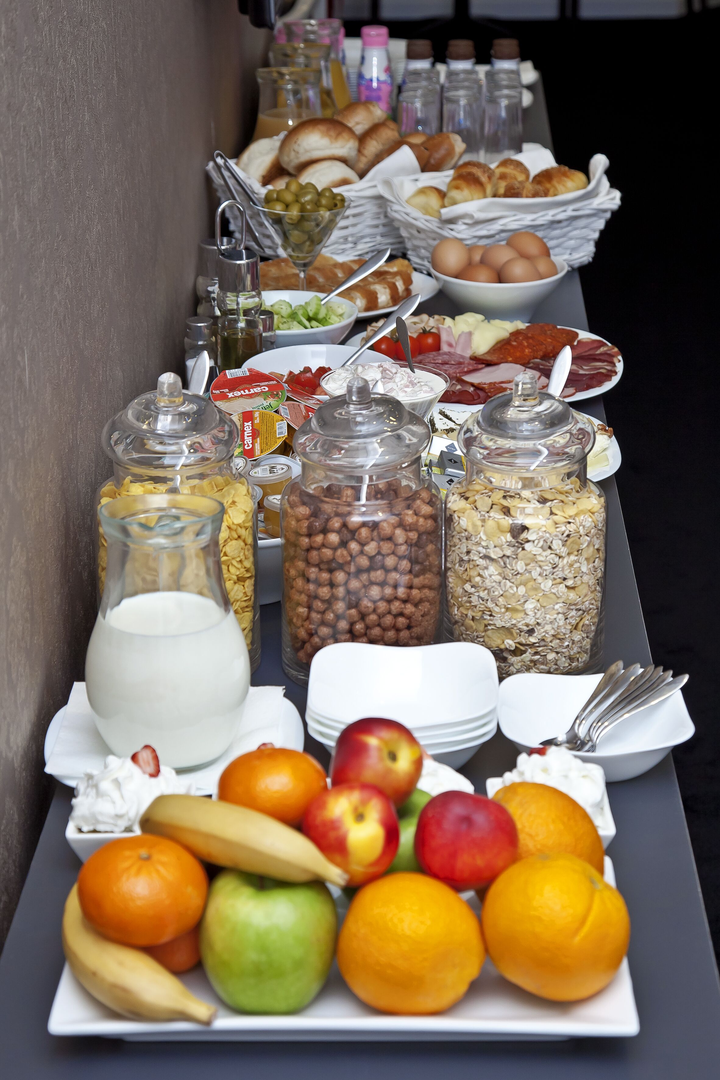 A buffet table with various food items including fruits, bread, and condiments.