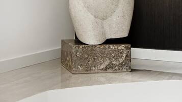 A sculpture of a female figure on a pedestal in a room with a dark wooden door and a white wall.