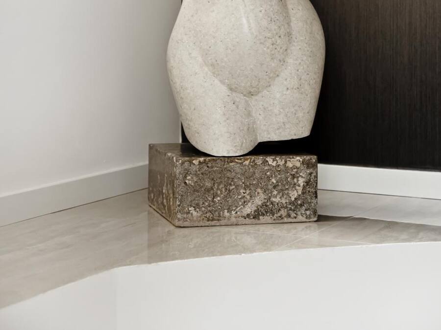 A sculpture of a female figure on a pedestal in a room with a dark wooden door and a white wall.