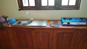 A kitchen with wooden cabinets, a stainless steel sink, and a blue gas stove. - The Sudbury Villa Nuwaraeliya (Nuwara Eliya)