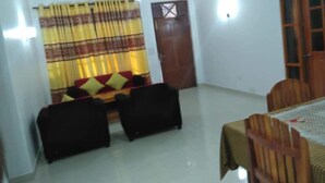 A dining area with a table and chairs, a sofa with cushions, and a door with a window. - The Sudbury Villa Nuwaraeliya (Nuwara Eliya)