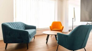 A modern living room with two teal armchairs, a round coffee table, and a bright orange chair.