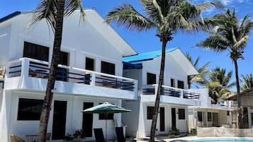 A modern two-story building with a swimming pool, palm trees, and a clear blue sky.