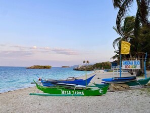 Een strand met boten, een bordje voor Tambisan Beach Boracay en palmbomen.