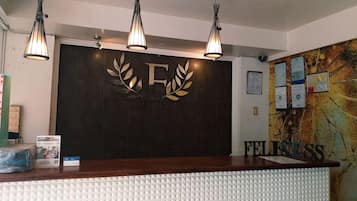 A reception desk with a dark wood finish, a white textured wall, and a large 'F' with a leaf design above it.