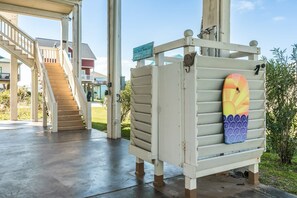 A covered outdoor area with a wooden staircase leading to a building, a surfboard leaning against a white structure, and a sign indicating a beach resort.