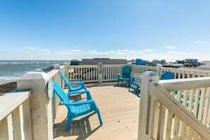 A wooden deck with blue chairs and a railing overlooking the ocean.