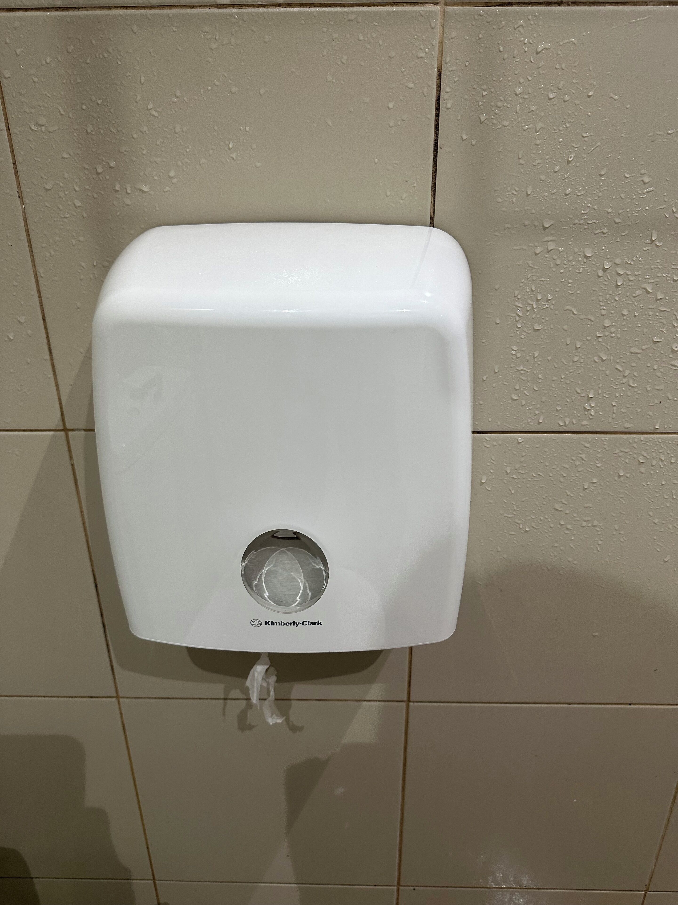 En hvid sæbedispenser fastgjort på en flisebelagt væg.