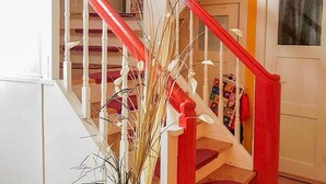 Una escalera con barandas blancas y detalles rojos que conduce a una puerta con un cuadro enmarcado.