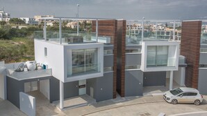 Ein modernes Wohngebäude mit Glasbalkon, einem geparkten Auto davor und freiem Blick auf die umliegende Nachbarschaft.