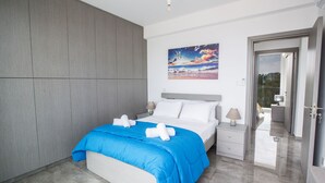 Ein modernes Hotelzimmer mit einem großen Bett, einem Gemälde an der Wand und Blick durch eine geöffnete Tür.