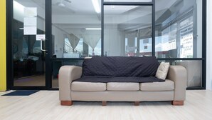 Un espacio de oficina moderno con un sofá de cuero color beige, paredes de vidrio y una zona de trabajo visible con escritorios y sillas.