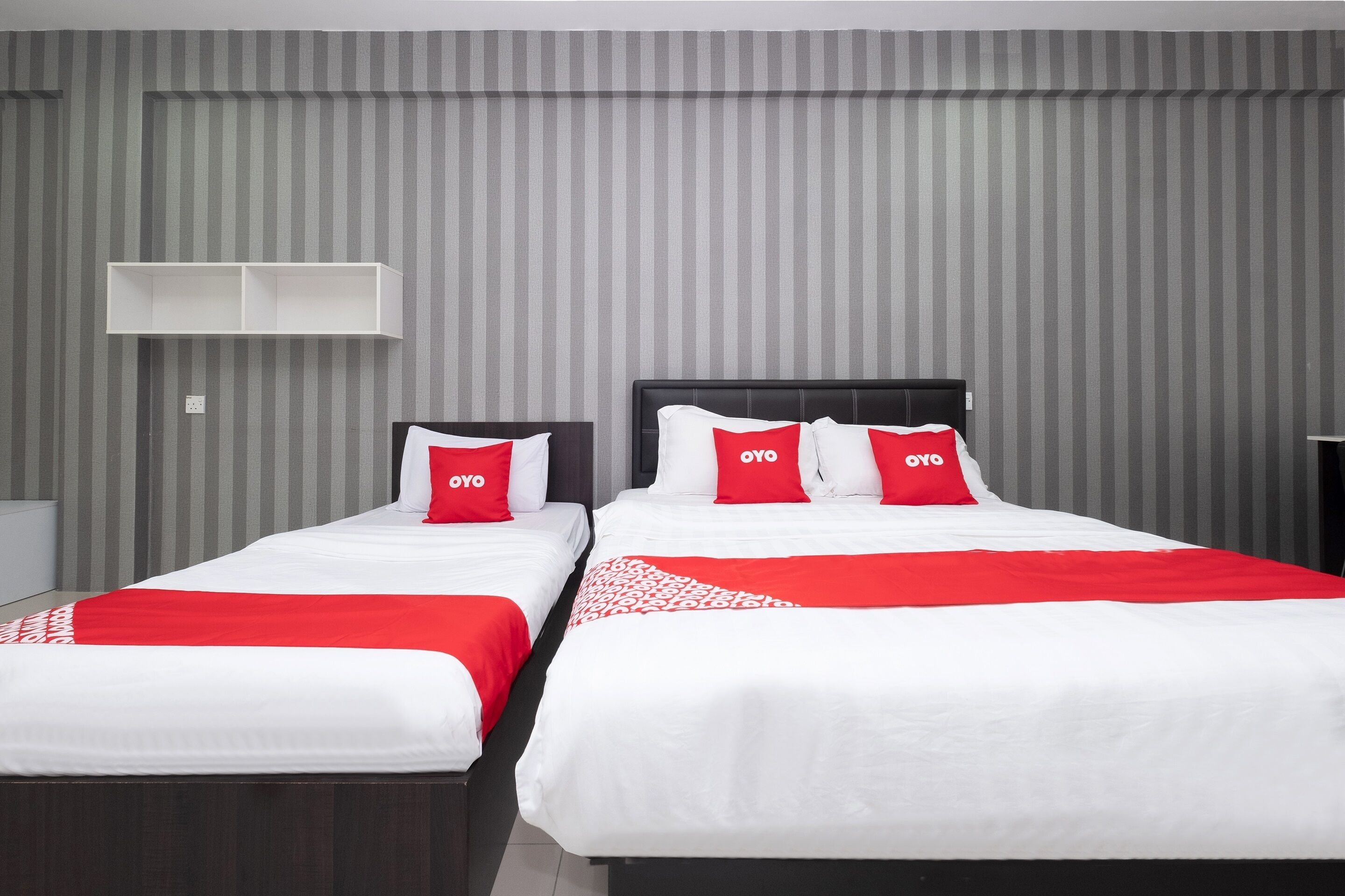 Habitación de hotel con dos camas, cada una con ropa blanca y detalles rojos, y una pared gris a rayas.
