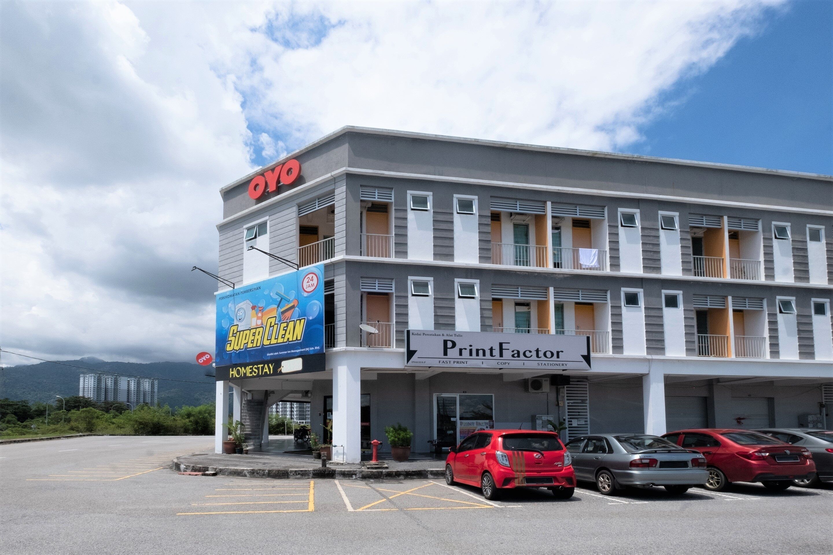 A multi-story building with a 'PrintFactor' sign, a 'Super Clean' advertisement, and several parked cars.
