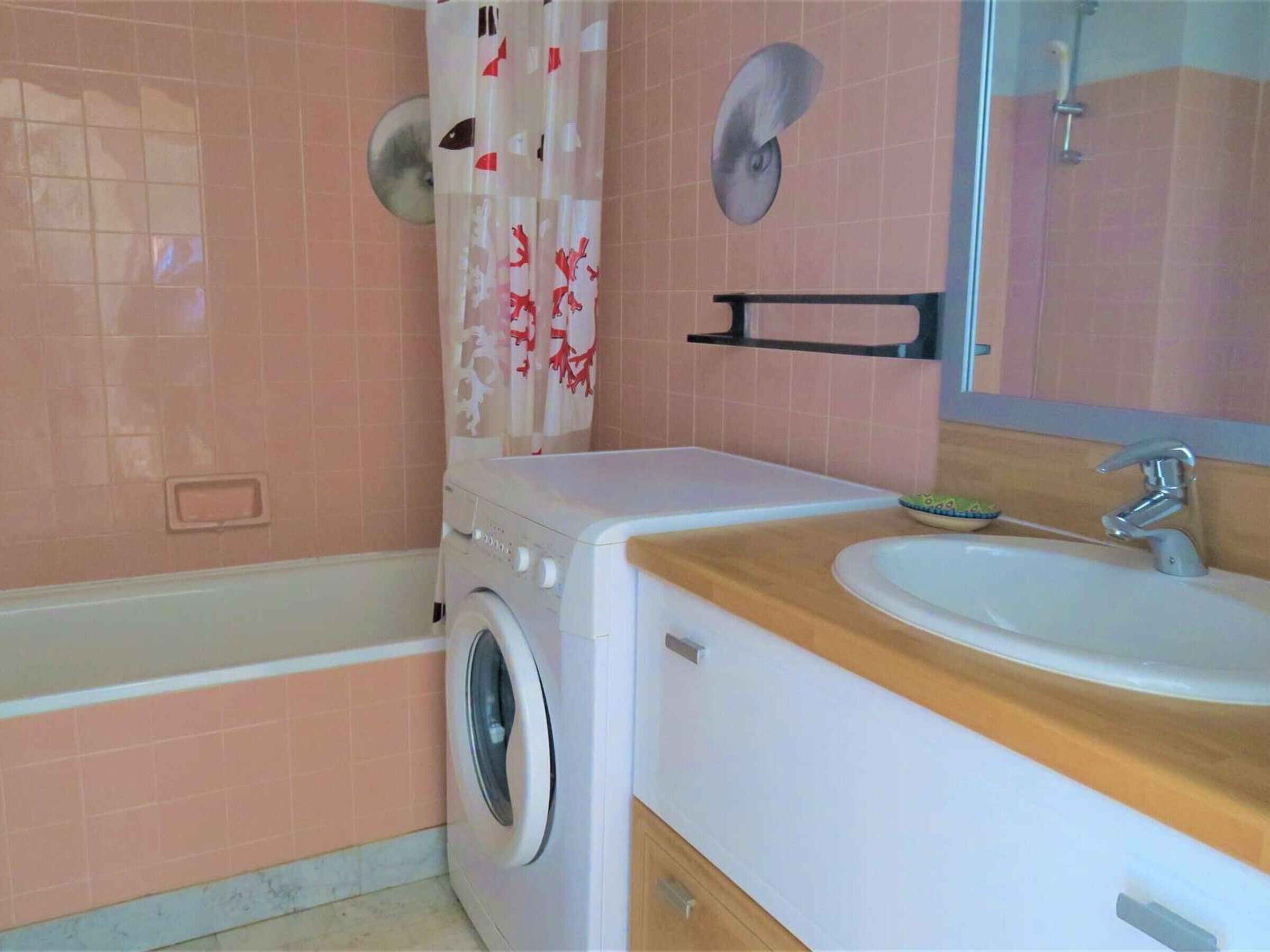 A bathroom with a washing machine, a sink, and a shower curtain.