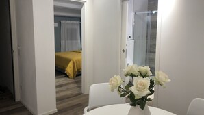 Une chambre d’hôtel avec un lit, une table blanche ornée d’un vase de fleurs et un espace douche.