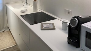 Une cuisine moderne avec des meubles blancs, une plaque de cuisson à induction noire, un four à micro-ondes et une machine à café.
