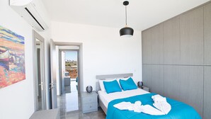 Un dormitorio moderno con una cama grande, una mesita de noche, una lámpara colgante y vistas a través de una puerta abierta.