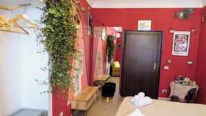 Una camera d'albergo con un letto, una panca, una scrivania, un armadio e una porta.
