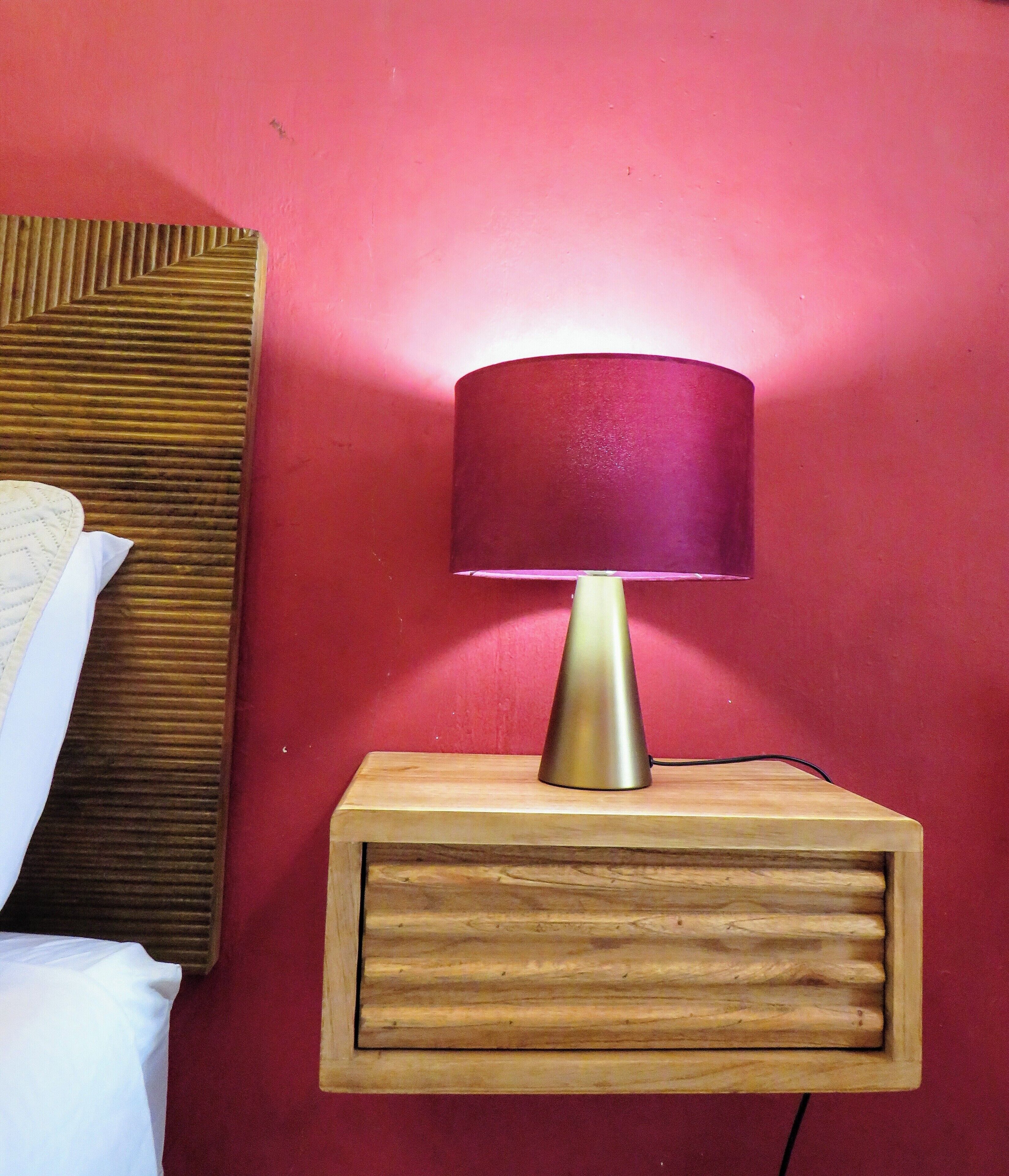 Ein Nachttisch aus Holz mit einer Lampe vor einer roten Wand.