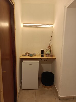 Ett litet, praktiskt kök med ett kylskåp, en arbetsbänk med diverse föremål och en liten papperskorg.