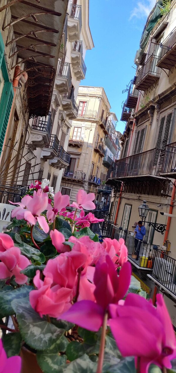 A narrow street with buildings on either side, balconies, and a clear blue sky.