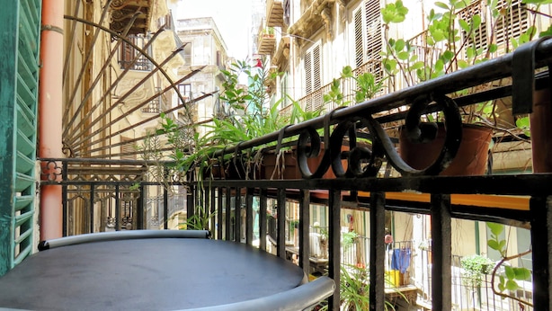 Un balcone con ringhiera in metallo, piante in vaso e vista sui palazzi vicini.