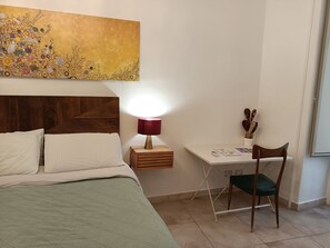 Ett hotellrum med en säng, ett skrivbord, en stol, en lampa och en tavla på väggen.