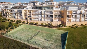 A multi-story hotel with balconies, a tennis court, and a landscaped area. - Flat Amora OCV - Ocean View (Albufeira)