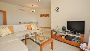 A living room with a sofa, coffee table, TV, and a bookshelf. - Flat Amora OCV - Ocean View (Albufeira)