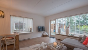 A spacious living room with a wooden floor, a sofa, a table, and a TV.